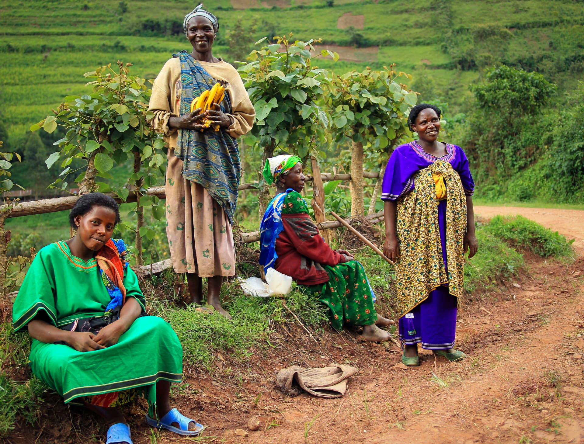 Women in colourful dress resting beside a road in the green hills of Uganda