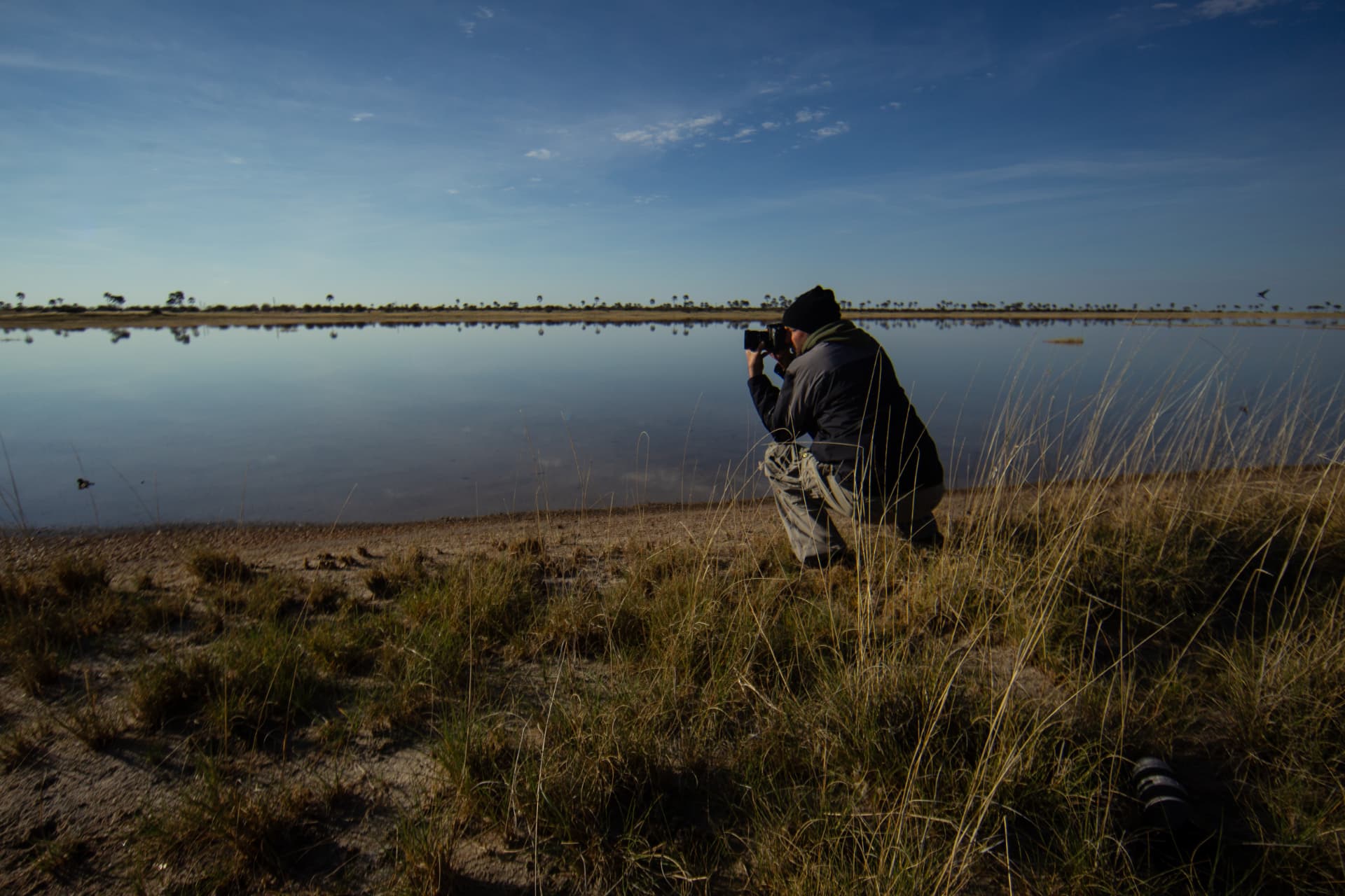 Photographer kneeling beside a mirror-still pan at dawn